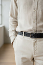 Handmade black leather belt with matte buckle, styled with beige pants and shirt, designer accessory by Fashion Racing.