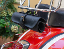 Black leather motorcycle tool roll securely fastened to the back of a red motorcycle Vespa. The handcrafted leather roll bag features a buckle closure and is neatly attached to the chrome frame behind the seat, ready for transport of tools