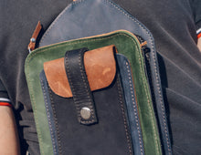Close-up of a handcrafted men's leather crossbody bag with green, brown, and black leather, detailed stitching, and an adjustable strap with a sturdy buckle,