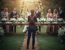 Wedding photographer wearing a personalised brown leather dual camera harness with logo, capturing a couple during an outdoor wedding ceremony.