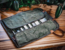 Handcrafted waxed canvas and leather knife roll bag open on wooden table with flap covers, chef knife storage slots visible