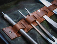 Detail of leather loops holding carving fork and sharpening steel inside waxed canvas chef knife roll