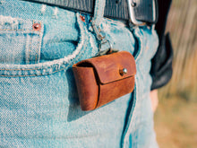 Handcrafted brown leather dog poop bag holder clipped to a belt loop. Stylish and durable pet accessory for dog owners who value fashion and functionality.