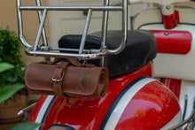 Brown leather motorcycle tool roll securely fastened to the back of a red motorcycle, neatly attached to the chrome frame behind the seat.