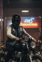 Motorcyclist wearing black and white café racer leather jacket sitting on motorcycle