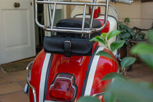 Black leather motorcycle tool roll fastened to the back of a red motorcycle, neatly attached to the chrome frame behind the seat. The tool roll features a buckle closure and is designed for convenient storage and transport of tools.