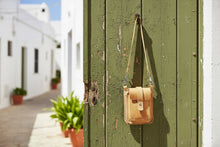 Yellow leather handcrafted women crossbody bag hanging on rustic green wooden door in Mediterranean alley.