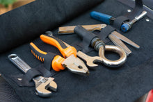 Close-up of an open black leather motorcycle tool roll with various tools including pliers, wrench, and screwdriver, neatly organized in their slots.