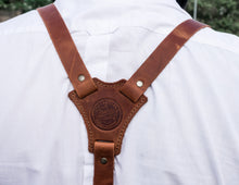 clear view of the back of the person wearing the brown leather suspenders. The intersection of the suspender straps is prominently shown, featuring the same leather patch with the brand logo "Fashion Racing Handmade Custom Leather"