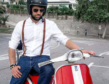 The fourth image shows a person sitting on a red and white Vespa scooter. They are wearing a white button-down shirt paired with brown leather suspenders and blue jeans. The person is also wearing a black helmet with a visor and aviator sunglasses, adding to the stylish, vintage-inspired look. The suspenders are prominently featured, providing a classic accessory that enhances the outfit's overall aesthetic.