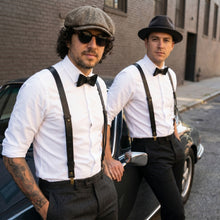 Two men in vintage  with leather suspenders and hats standing next to a car