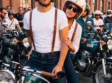 Man and woman in matching brown leather suspenders with brass clips at a cafe racer meet