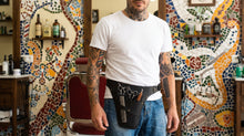 barbershop wearing a black leather barber tool belt with shears and other tools.