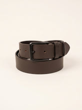 A dark brown leather belt with a matte black metal buckle, neatly coiled on a light cream background.