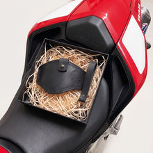 Black leather motorcycle boot protector and matching keychain presented in a gift box filled, displayed on the seat of a red Ducati 848 motorcycle