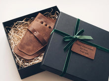 gift box featuring a handcrafted personalized leather tool holster nestled in natural wood shred packaging. The premium full-grain leather pouch is presented in elegant gift-ready packaging with a black gift box, green velvet ribbon, and a custom engraved leather anniversary message tag reading, "Happy Anniversary, my love. – Your Wife." Designed to organize essential tools, this versatile leather holster is ideal for barbers, hairstylists, florists, gardeners, and other skilled professionals 