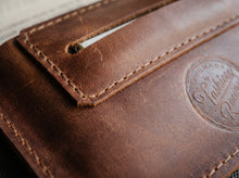 Handmade brown leather tobacco pouch with stitched edges and built-in rolling paper holder
