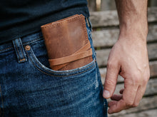 Handmade brown leather tobacco pouch with wraparound strap, shown in a jeans pocket