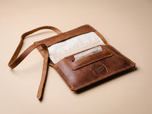 Handmade brown leather tobacco pouch with long leather strap, rolling paper compartment, and built-in paper holder, shown open