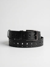 A black perforated leather belt with a dark metal buckle, coiled on a light gray background.