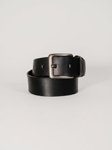 A black leather belt with a silver-toned metal buckle, neatly coiled on a light gray background.