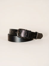 A black leather belt with a dark metal buckle, neatly coiled on a light beige background.