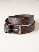 A dark brown leather belt with a geometric pattern of lighter brown lines and a silver-tone metal buckle, coiled on a light beige background.