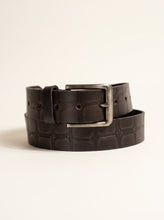 A dark brown embossed leather belt with a silver-tone metal buckle, neatly coiled on a light beige background.