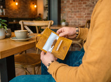 Handmade mustard-yellow leather tobacco pouch with rolling tobacco and paper holder, shown open.
