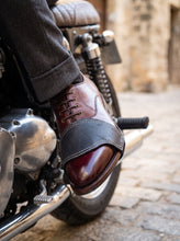 Close-up of black leather motorcycle shifter boot protector. A close-up of a person's leg resting on a motorcycle, wearing a brown leather motorcycle shifter boot cover 