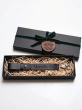 Personalized black Leather Glove Strap Holder engraved with the name  and presented in a premium black gift box with a green ribbon and custom leather anniversary gift tag. Handmade genuine leather glove holder featuring a secure belt loop, adjustable strap, and swivel snap hook. A personalized gift for motorcycle riders, bikers, husbands, Father's Day, anniversaries, birthdays, Christmas, and everyday carry (EDC) enthusiasts.