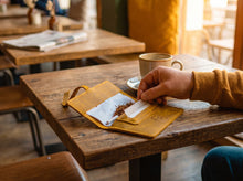 Handmade mustard-yellow leather tobacco pouch with rolling tobacco and built-in paper holder, shown open