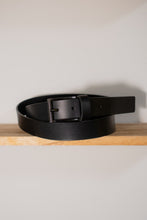Black minimalist leather belt with metal buckle on wooden table