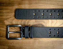 Black leather belt with perforated pattern and silver buckle laid flat for close-up detail.