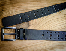 Black leather belt with perforated rows and brushed metal buckle shown in a flat lay.