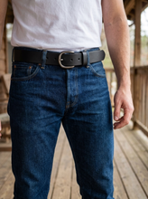 Black leather belt with rounded buckle worn with dark blue jeans for casual style