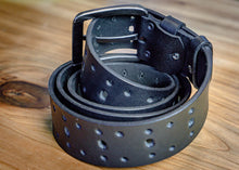 Black perforated leather belt coiled to highlight its buckle, stitching, and adjustable design