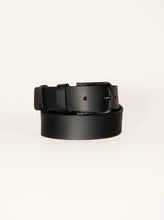 A black leather belt with a matte black metal buckle, neatly coiled on a clean, light off-white background.
