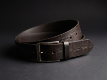 Dark brown crocodile-textured leather belt with metal buckle coiled for a premium product close-up