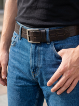 Dark brown crocodile-textured leather belt with silver buckle worn with blue jeans.