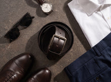 Dark brown embossed leather belt with silver buckle styled with white shirt and navy trousers.