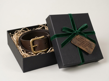 A brown leather belt with a gold-tone buckle presented in an open black gift box with gift message