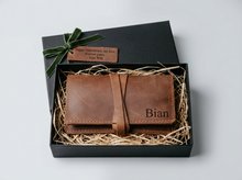 Personalized brown leather tobacco pouch in an open black gift box with shredded paper filler, green velvet ribbon, and an anniversary gift tag reading “Happy Anniversary, my love. Forever yours. – Your Wife.”