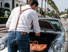 A man in a white shirt and blue jeans with brown suspenders