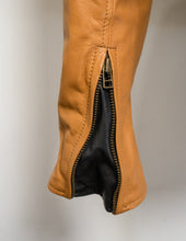 Close-up of a tan leather boot with a zipper on a neutral background