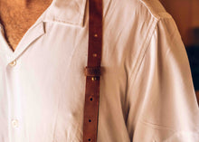 A close-up of a person wearing a white button-up shirt and a brown leather suspenders,