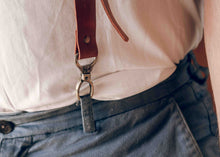 Close-up of a person wearing brown leather suspenders with metal snap hook attached near the waistband.