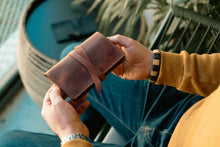 A person holding a dark brown leather tobacco rolling pouch 