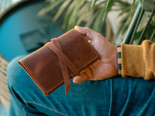 closed brown leather tobacco pouch with a wraparound leather strap, showing hand-stitched edges and a rustic finish