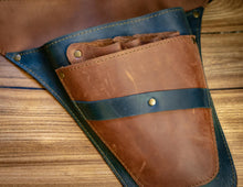 A close-up of a brown leather tool belt pouch or holster with a dark blue leather strap and brass snap